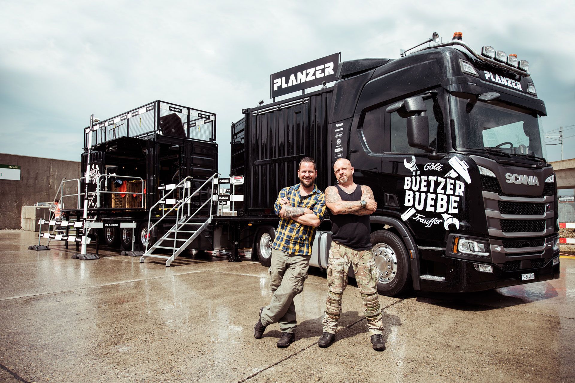 Göle & Trauffer stehen vor dem Planzer Event-Truck mit aufgebauter B\u00fchne und Sound-Equipment im Hintergrund.