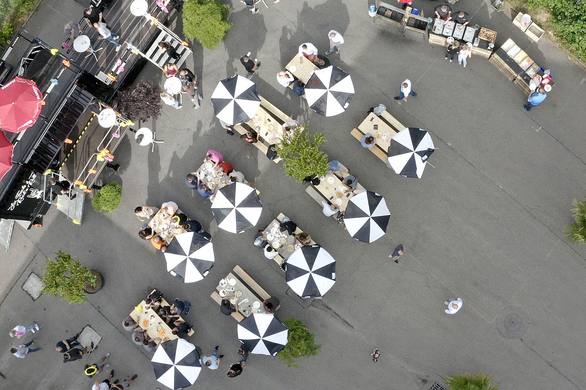 Luftaufnahme eines Outdoor-Events mit Planzer Event-Truck, Besuchern an Tischen und einem lebendigen Marktplatz-Setting.