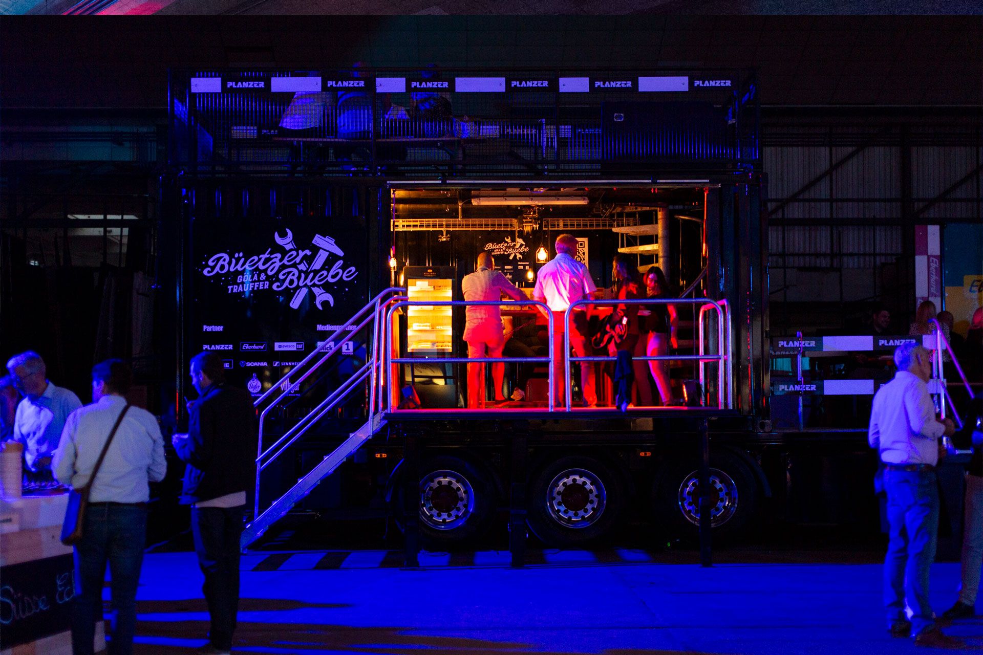 Besucher interagieren und geniessen eine Veranstaltung auf dem beleuchteten Event-Truck bei Nacht.