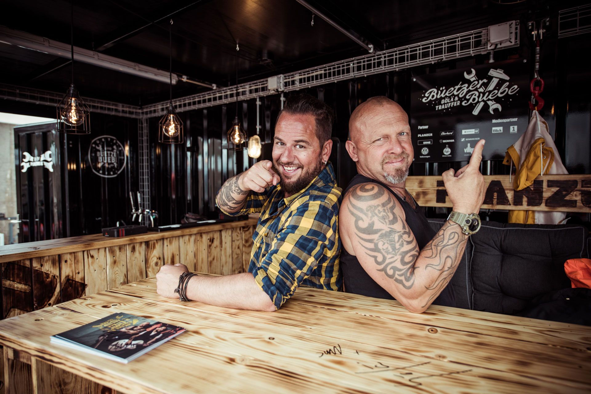 Gölä & Trauffer an der Bar im Inneren des Event-Trucks, mit einem stimmungsvoll beleuchteten Interieur im Hintergrund.